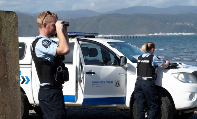 2 MPI fishery officers in uniform looking through binoculars on the coast.